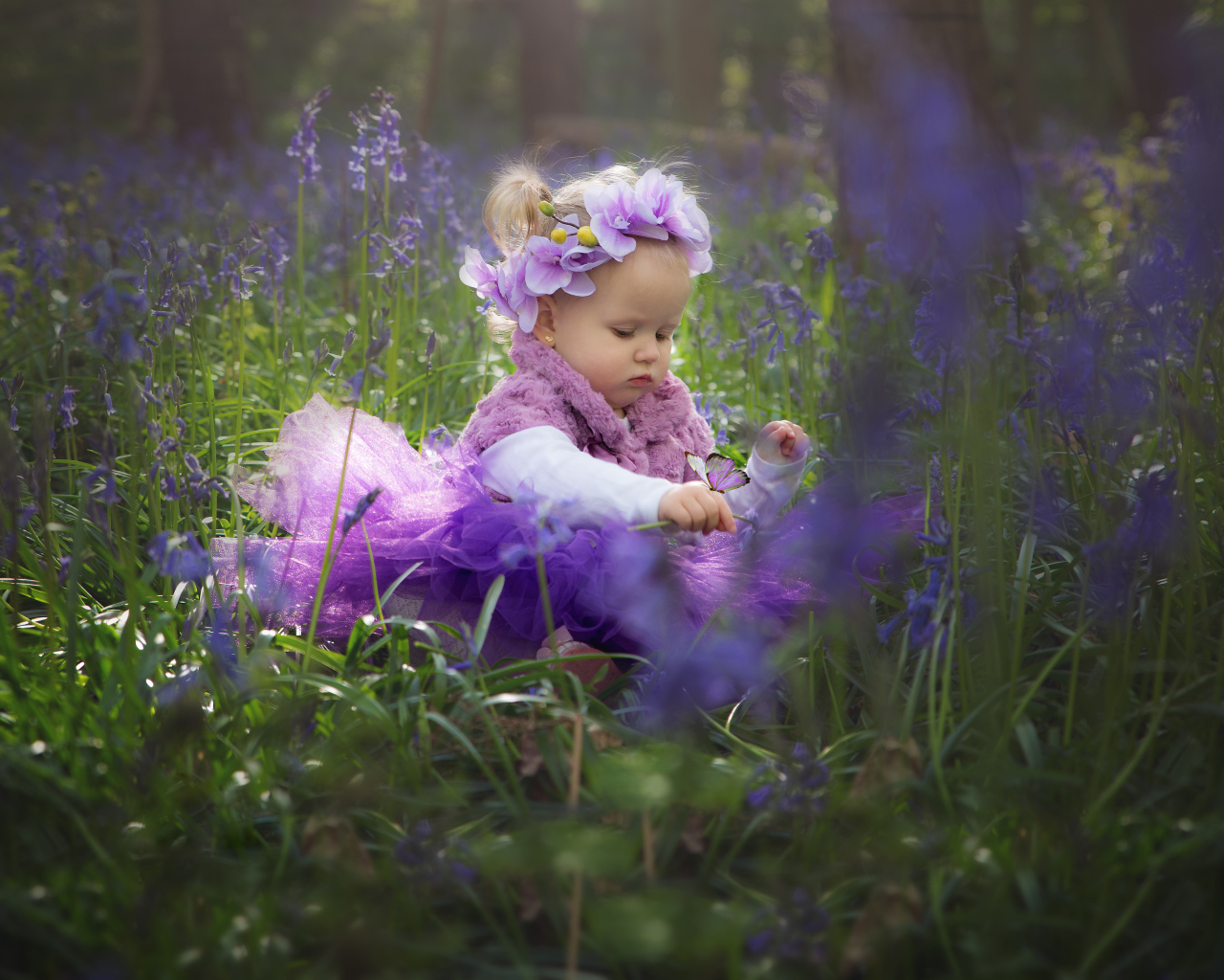 Маленькая девочка в красивом платье сидит в цветах с бабочкой на руке