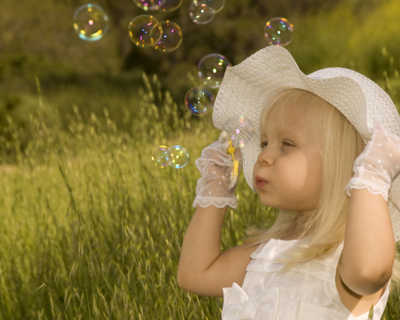 Маленькая девочка в большой белой шляпе пускает мыльные пузыри