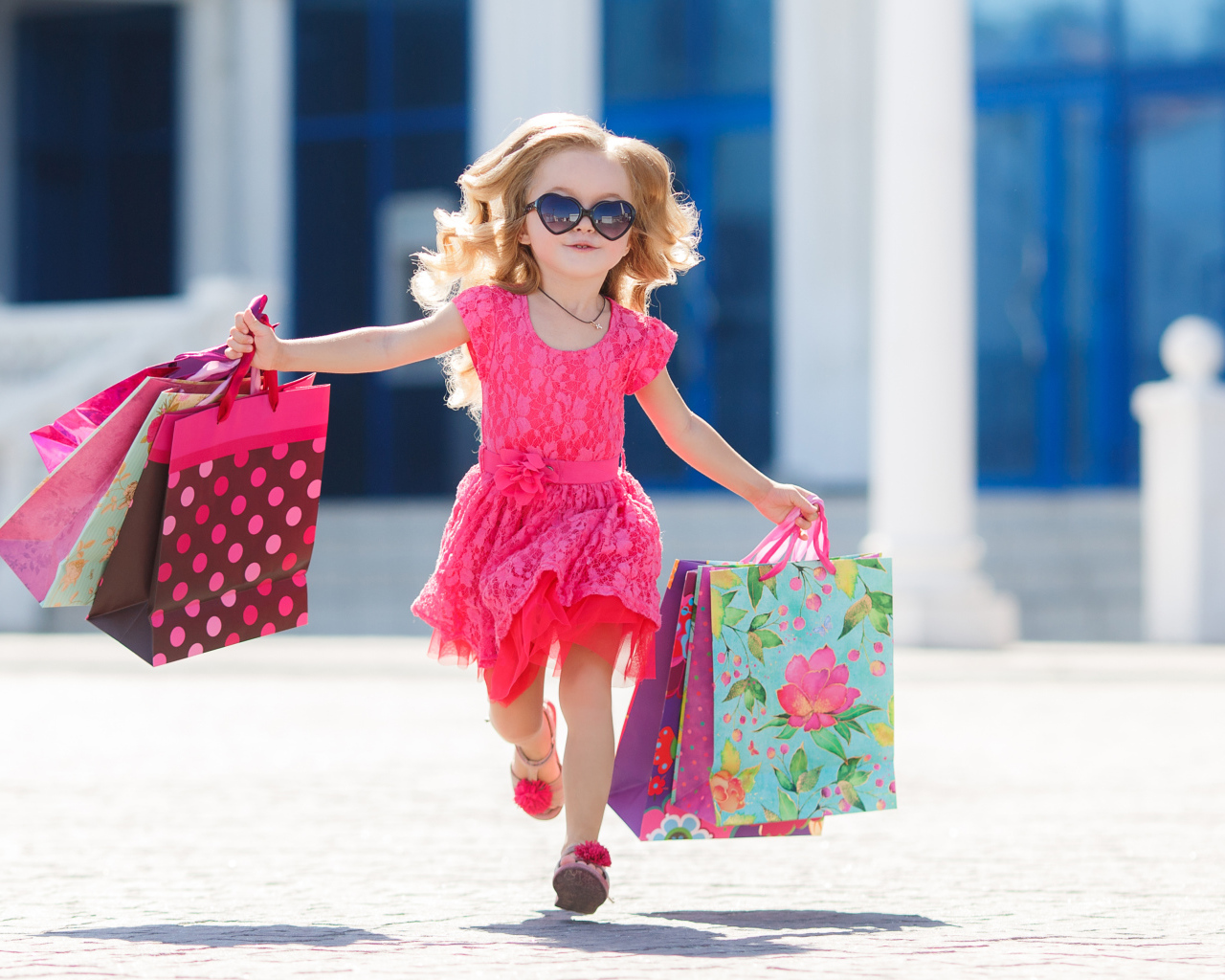 Маленькая девочка в розовом платье бежит с покупками из магазина