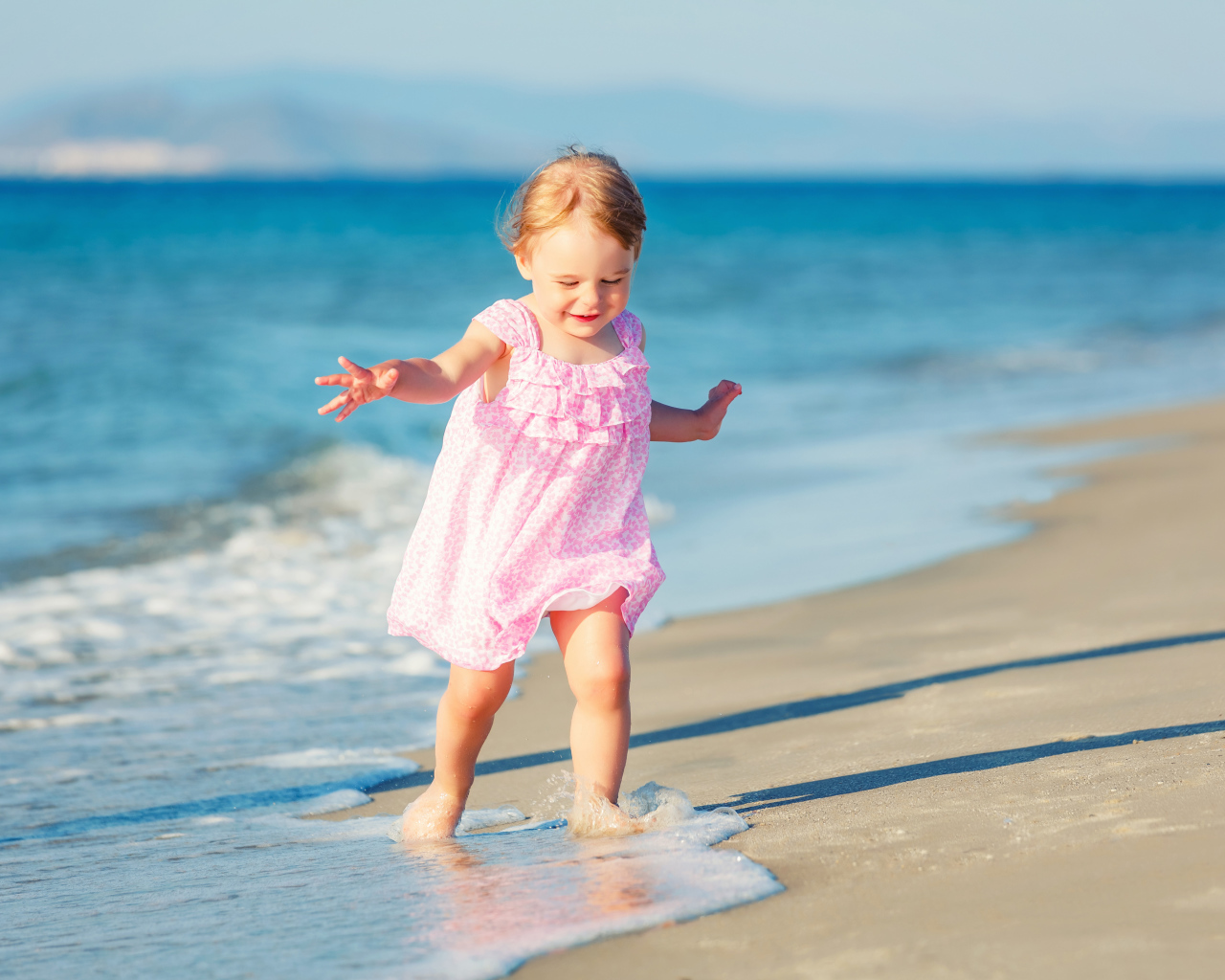 Маленькая девочка в розовом платье гуляет по морскому песку
