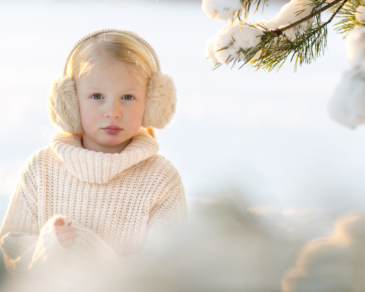Маленькая девочка в белом свитере у покрытой снегом ели