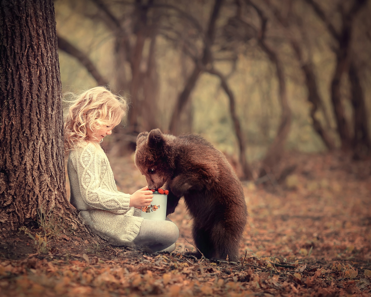 Маленькая девочка сидит у дерева с медвежонком гризли