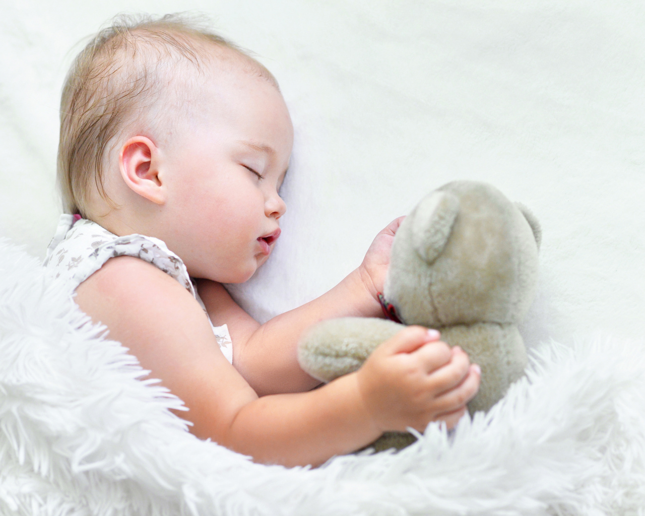 Маленькая девочка спит с мягкой игрушкой под белым одеялом