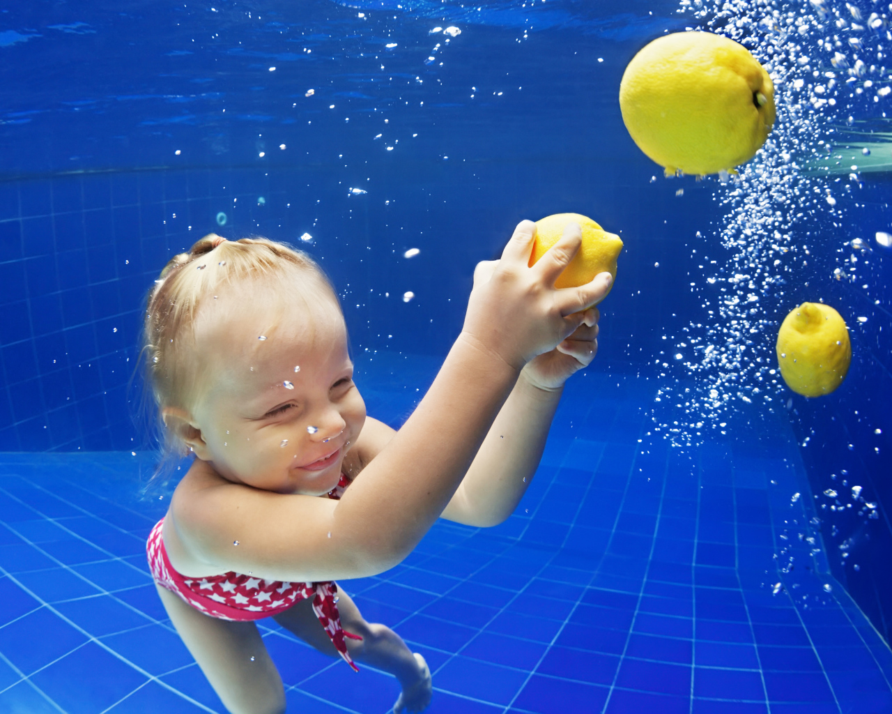 Маленькая девочка плавает в бассейне с желтыми лимонами