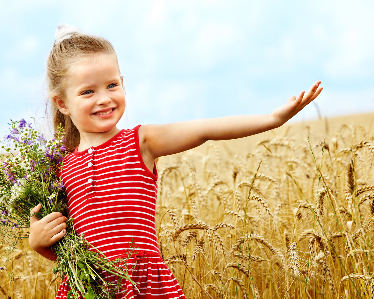 Маленькая девочка с букетом полевых цветов гуляет по полю пшеницы