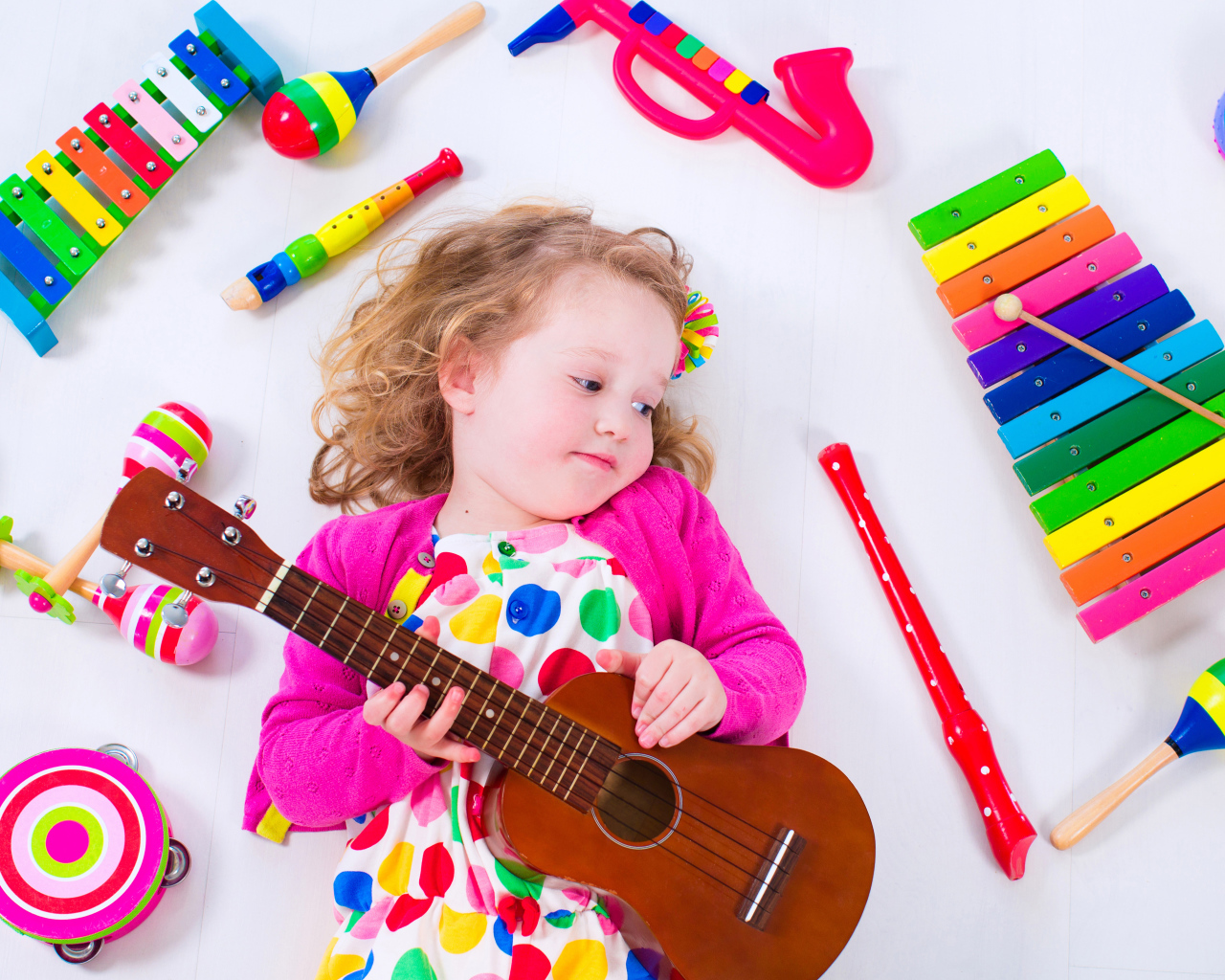 Маленькая девочка с гитарой лежит рядом с детскими музыкальными инструментами