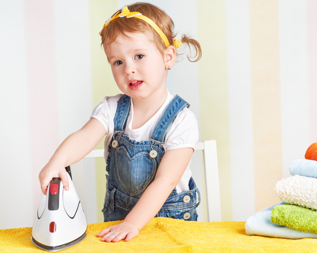 Маленькая девочка с утюгом гладит полотенце