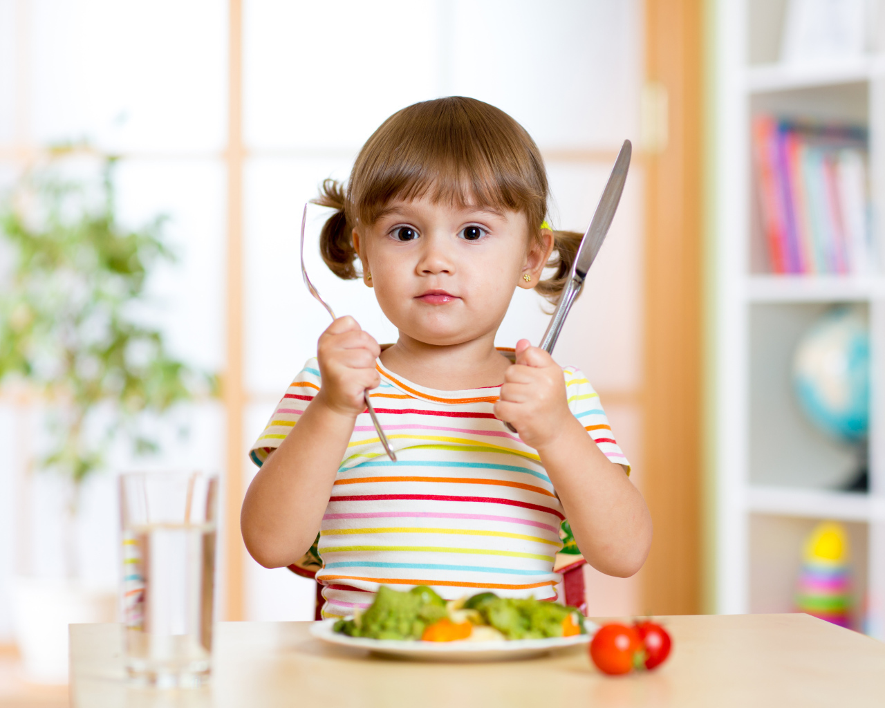 Маленькая девочка со столовыми приборами и тарелкой