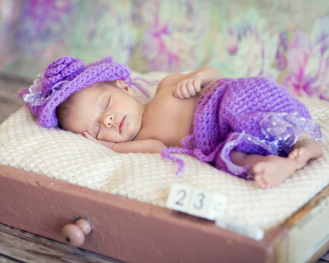 Маленький спящий младенец в вязаном фиолетовом костюме