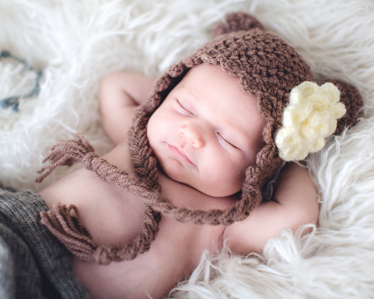 Спящий грудной ребенок в коричневой вязаной шапке с белым цветком