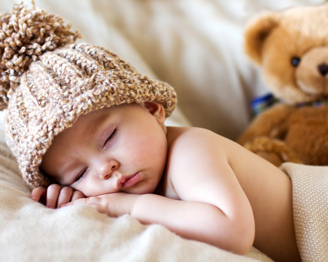 Спящий грудной ребенок в шапке с плюшевым мишкой
