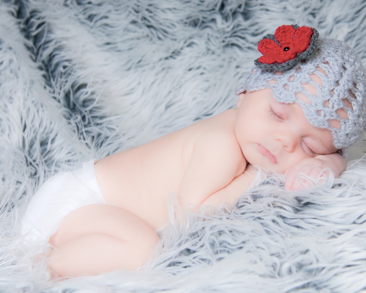 Спящий грудной ребенок в вязаной шапке с красным цветком на голове