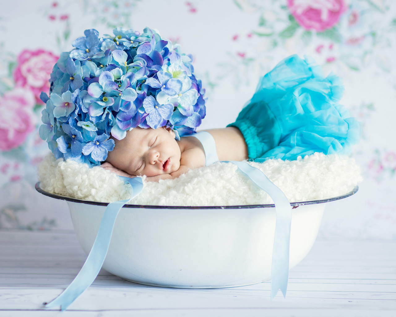 Маленький грудной ребенок спит в миске с шапкой из цветов гортензии на голове