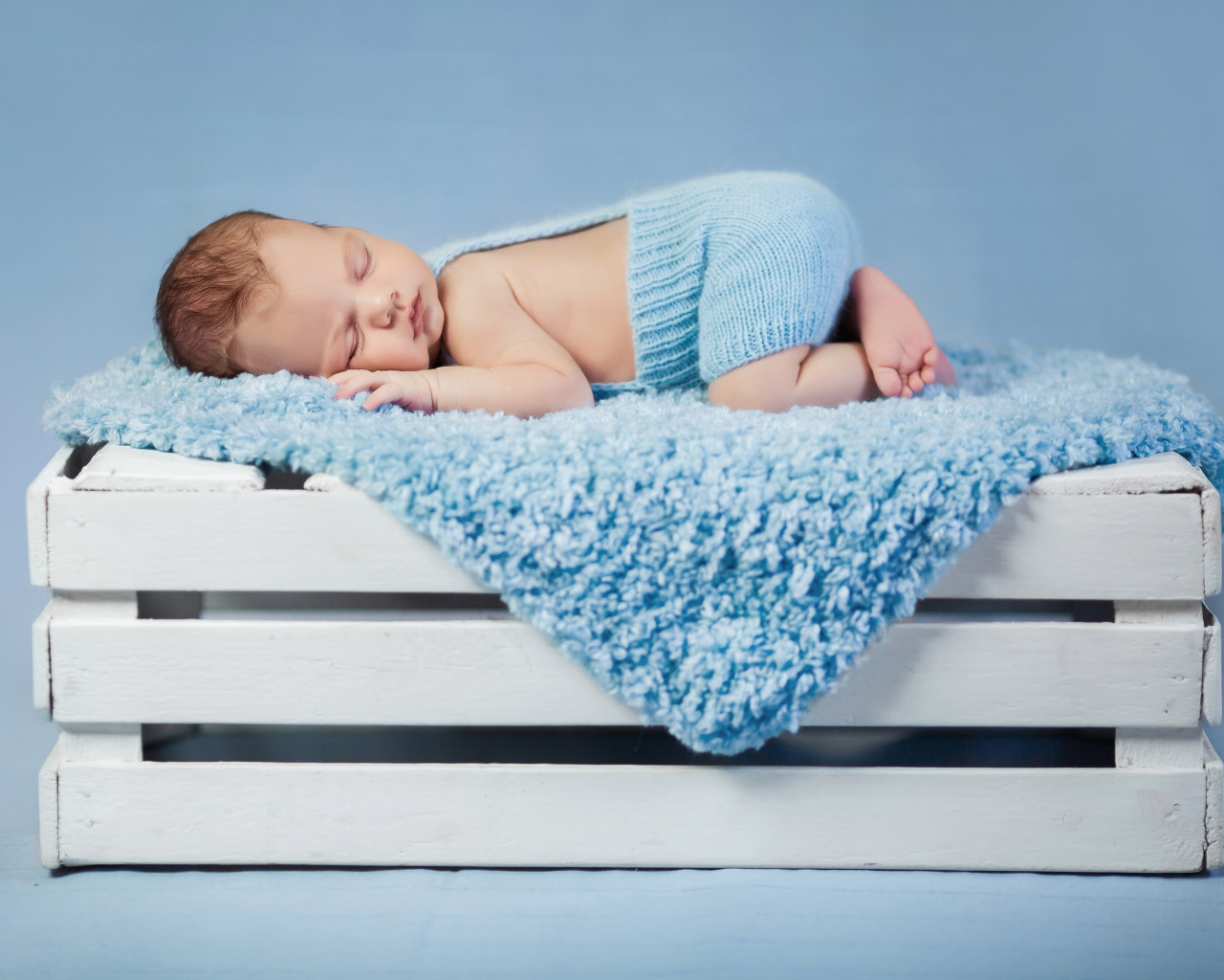 Маленький грудной ребенок спит на синем покрывале на деревянном ящике