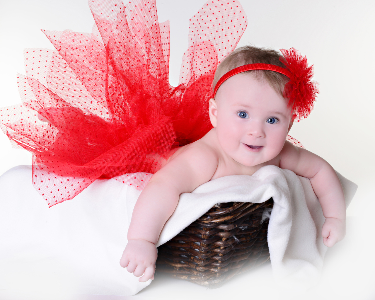 Маленькая голубоглазая девочка в красном красивом платье лежит в корзине