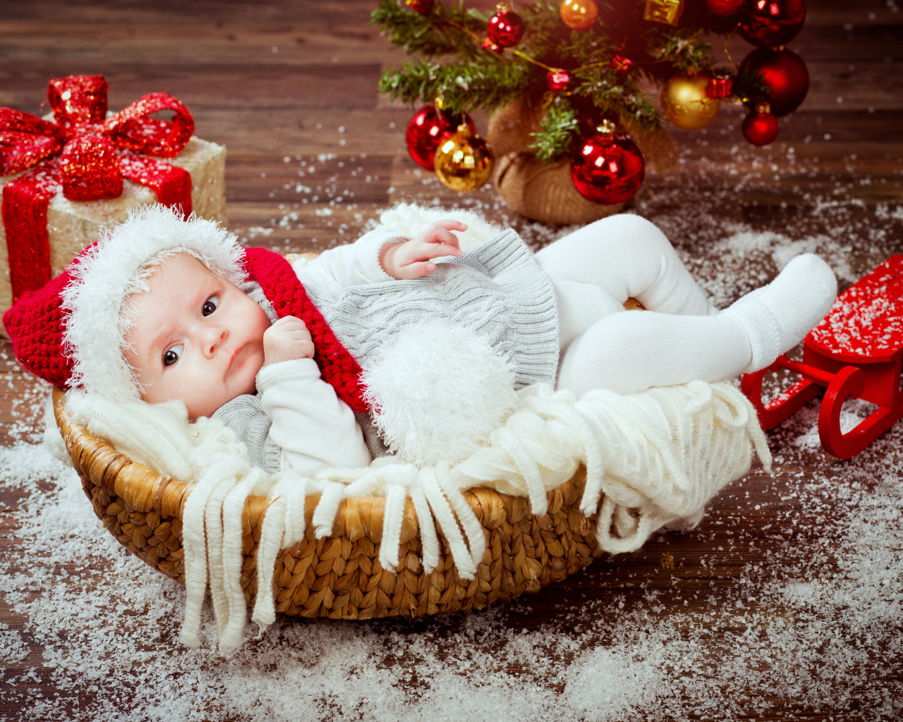 Младенец в корзине в новогоднем костюме под елкой с подарками