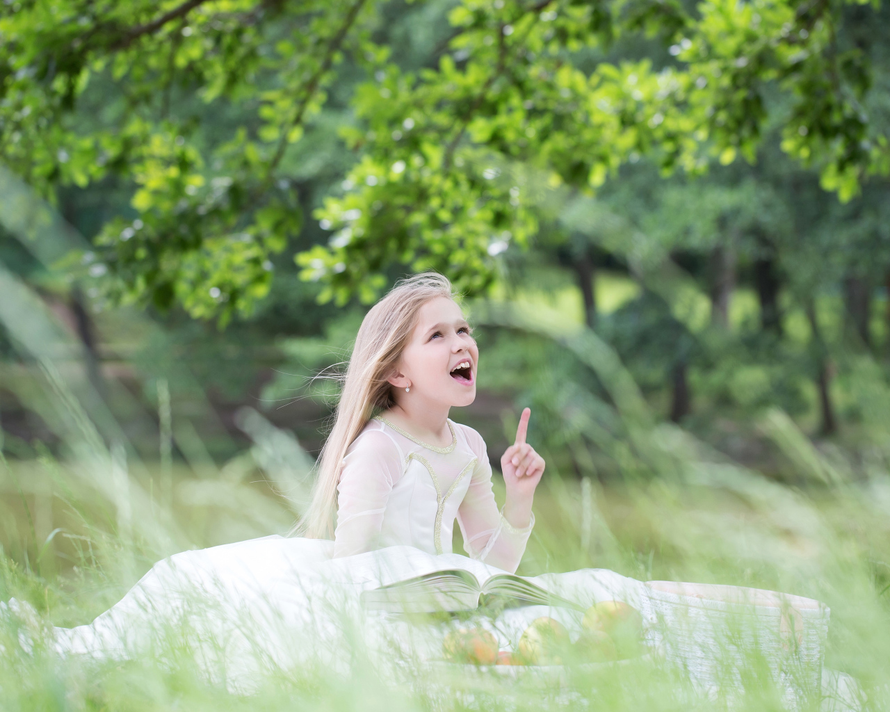 Красивая маленькая девочка в белом платье с книгой сидит на траве