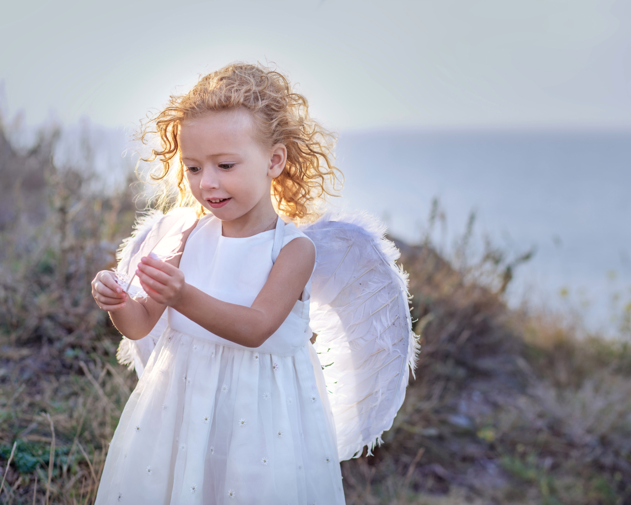 Красивая маленькая девочка в белом платье с крыльями ангела