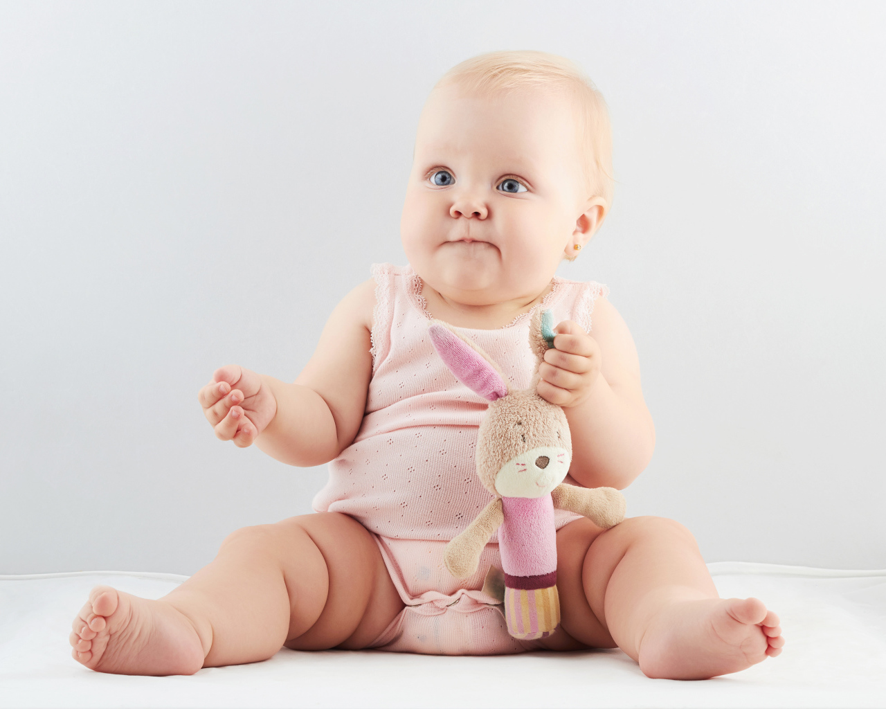 Голубоглазый младенец с мягкой игрушкой на сером фоне