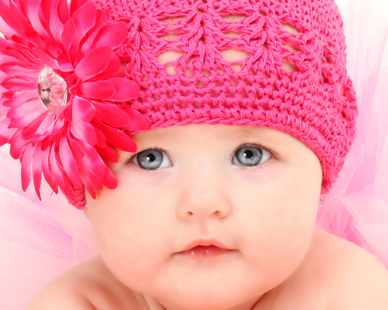 Милая голубоглазая малышка в розовой шапке с цветком герберы