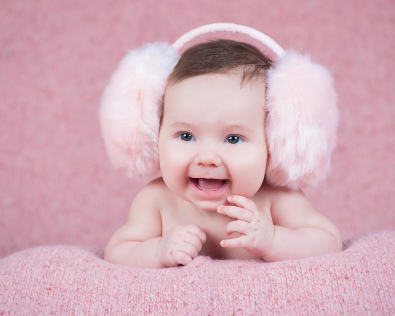 Милый улыбающийся младенец в больших розовых наушниках