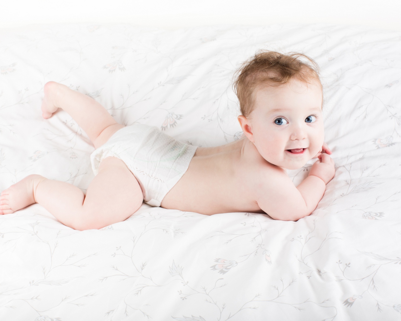 Забавный голубоглазый малыш лежит на белом покрывале