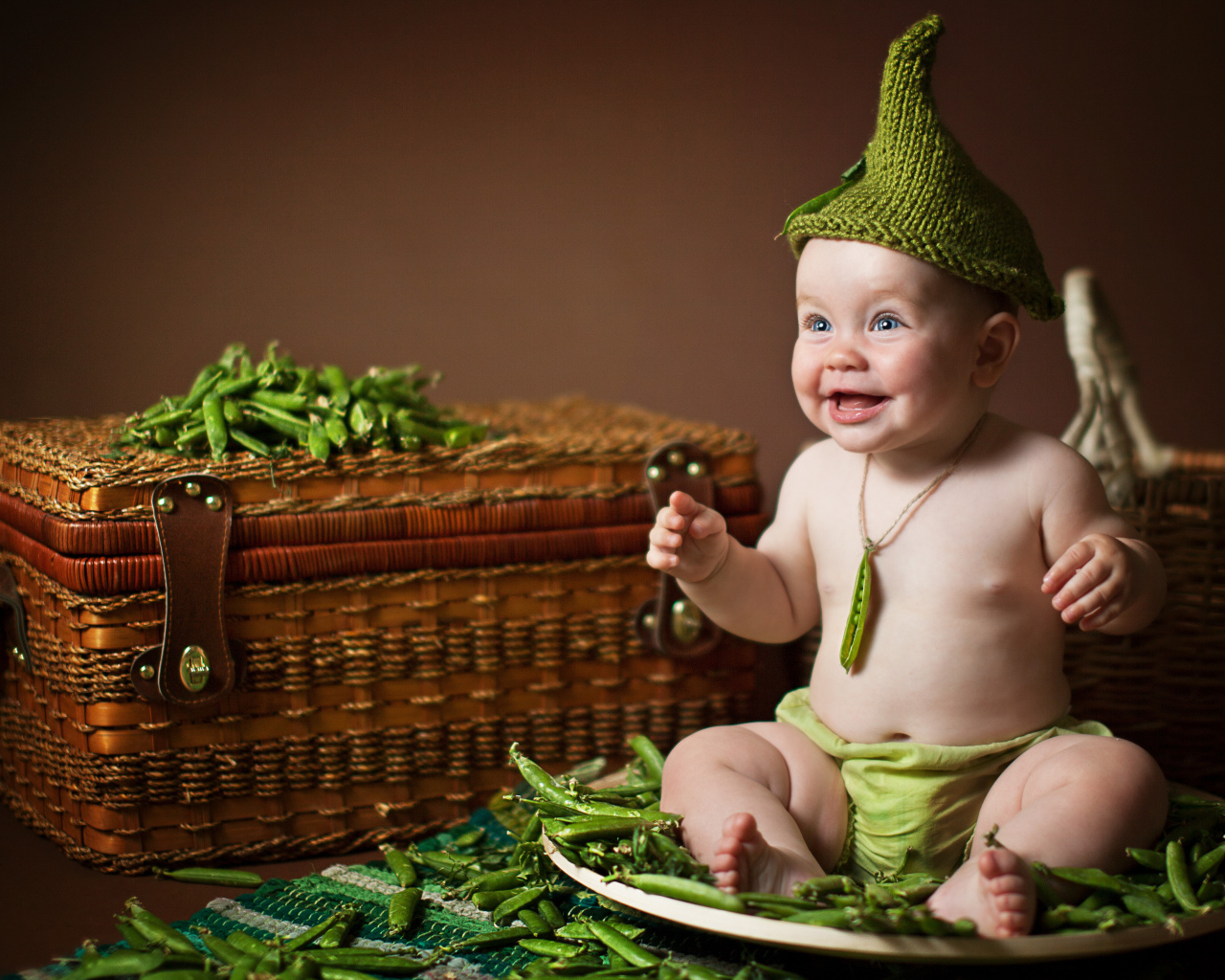 Забавный улыбающийся малыш сидит на стручках зеленого гороха