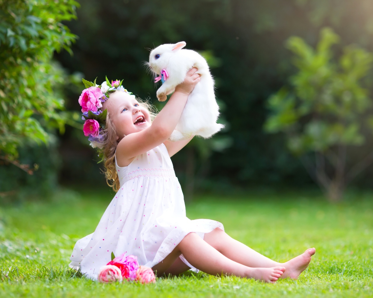 Радостная маленькая девочка в белом платье с кроликом в руках