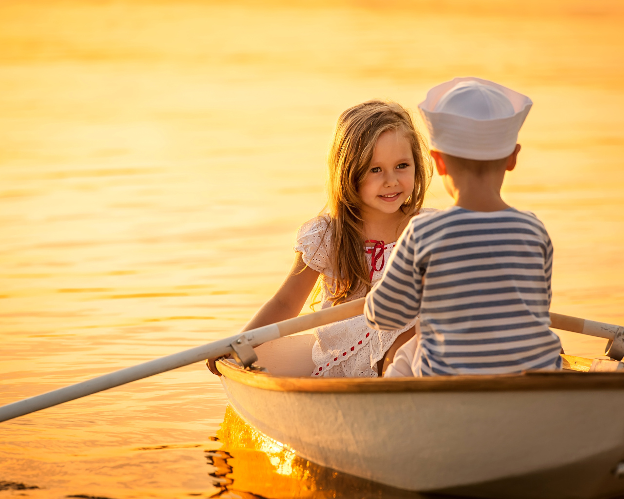 Маленькие мальчик и девочка плывут в лодке на закате солнца