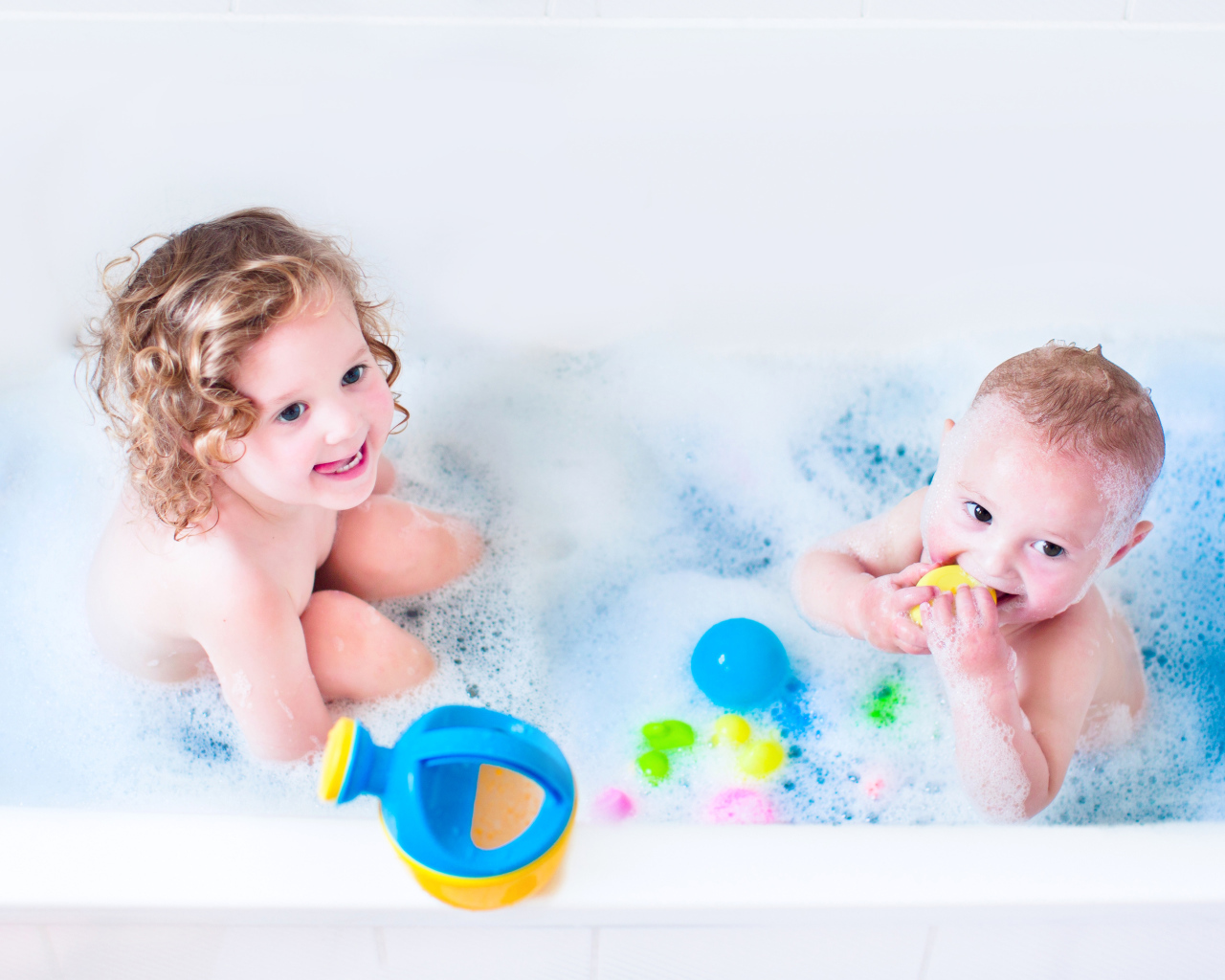 Маленькие мальчик и девочка купаются в ванной с игрушками