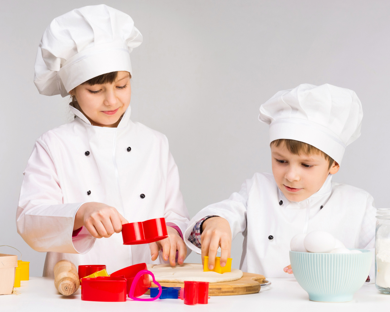 Маленькие мальчик и девочка готовят на кухне печенье