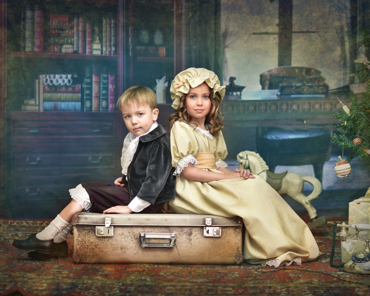 Маленькие мальчик и девочка в винтажных костюмах сидят на чемодане