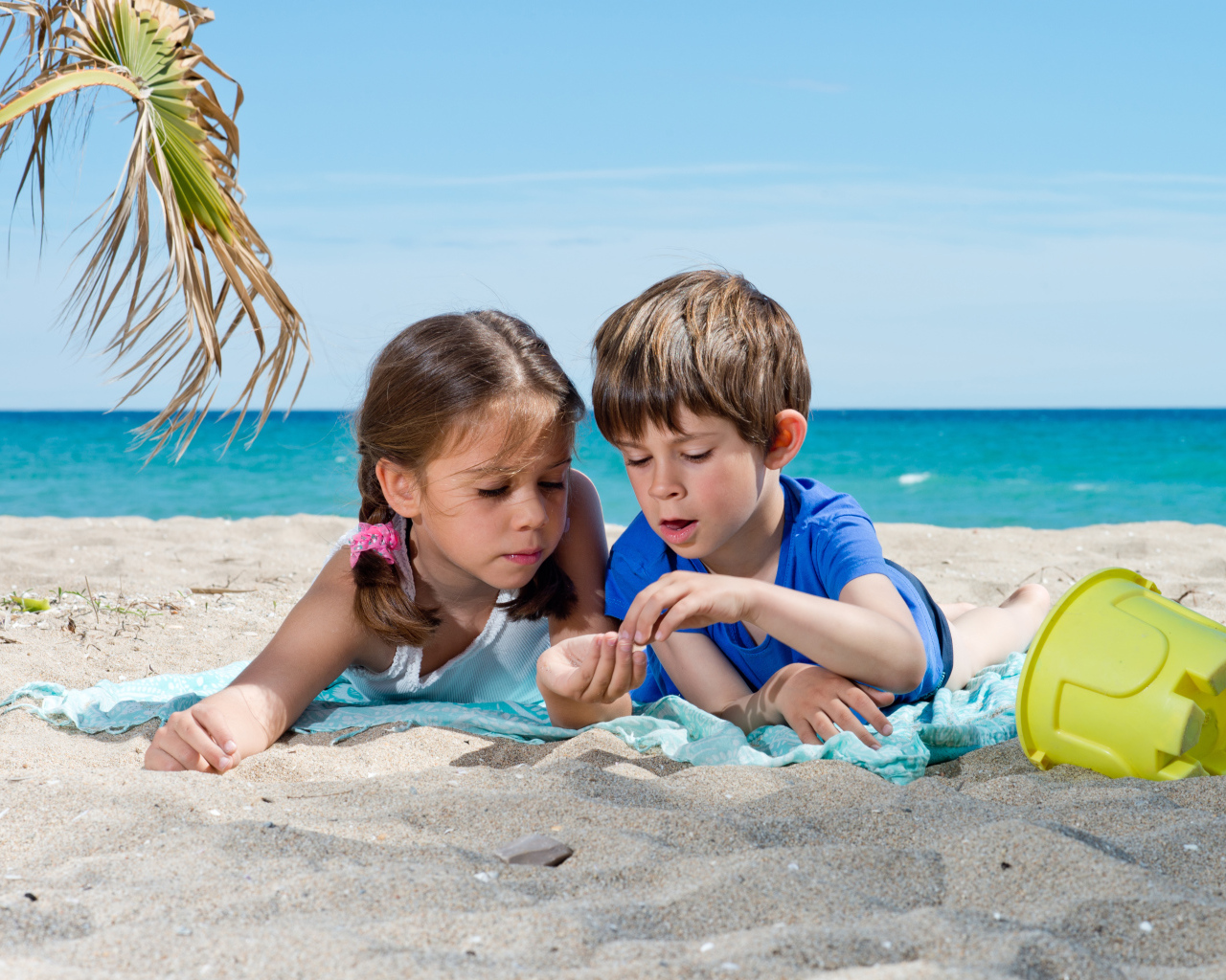 Маленькие мальчик и девочка играют на песке у моря