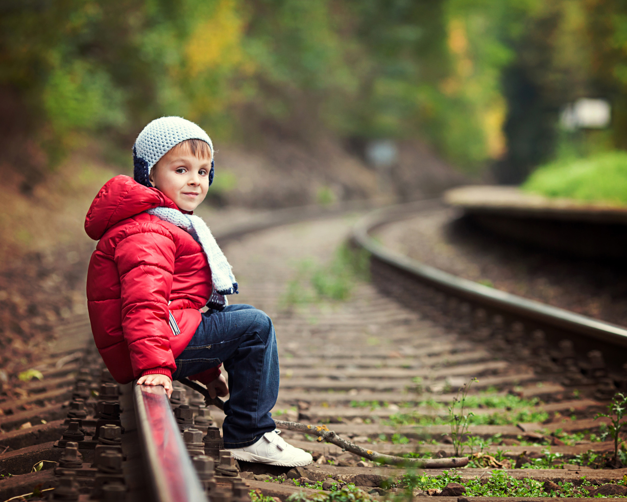 Маленький мальчик в красной куртке сидит на рельсах