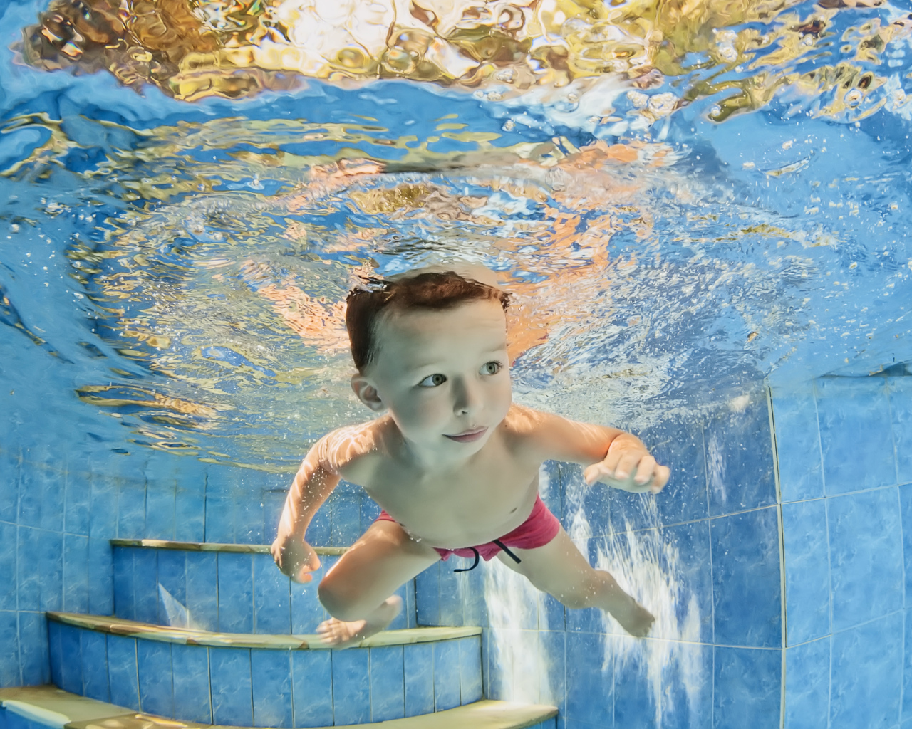 Маленький мальчик плавает под водой в бассейне