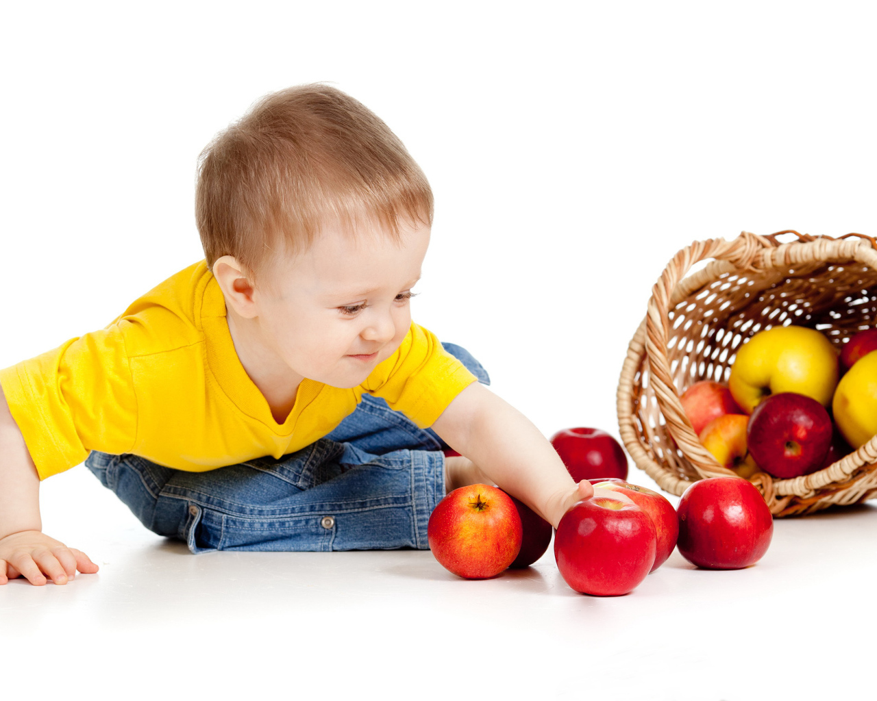 Маленький мальчик с корзиной спелых яблок на белом фоне