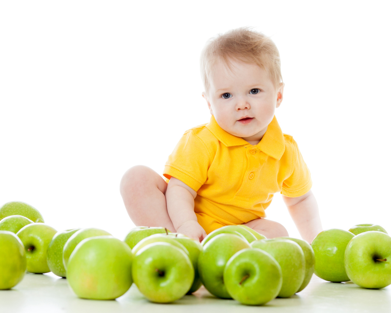 Маленький мальчик с зелеными яблоками на белом фоне