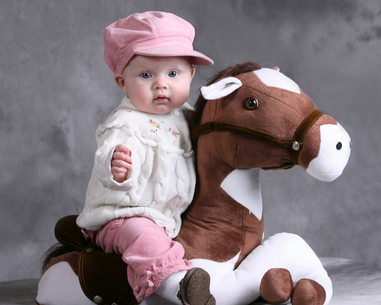 Маленький ребенок в розовой кепке сидит на игрушечной лошади