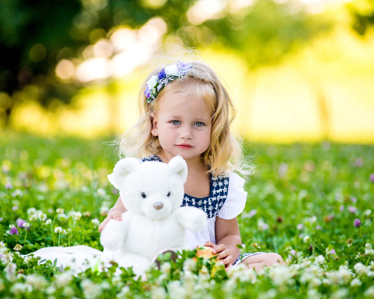 Маленькая милая девочка с игрушкой сидит на зеленой траве с цветами