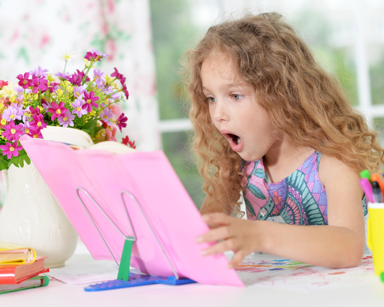 Маленькая русоволосая девочка удивленно смотрит в книгу