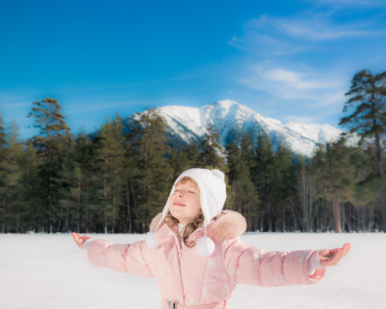 Маленькая девочка в розовой куртке на фоне гор зимой