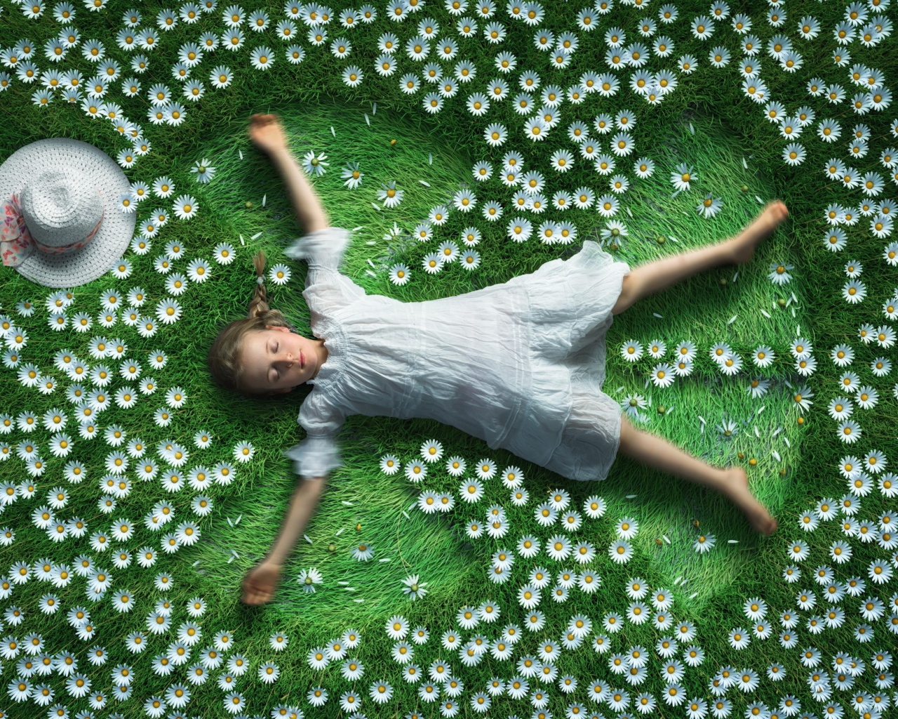 Маленькая девочка в белом платье лежит на зеленой траве с ромашками