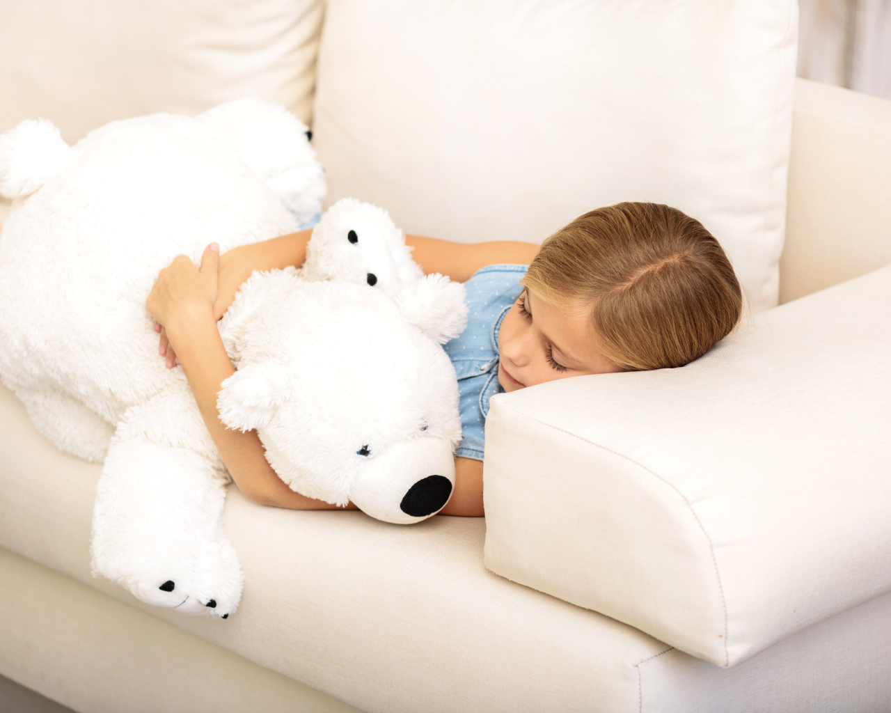 Маленькая девочка спит с белым плюшевым мишкой на диване