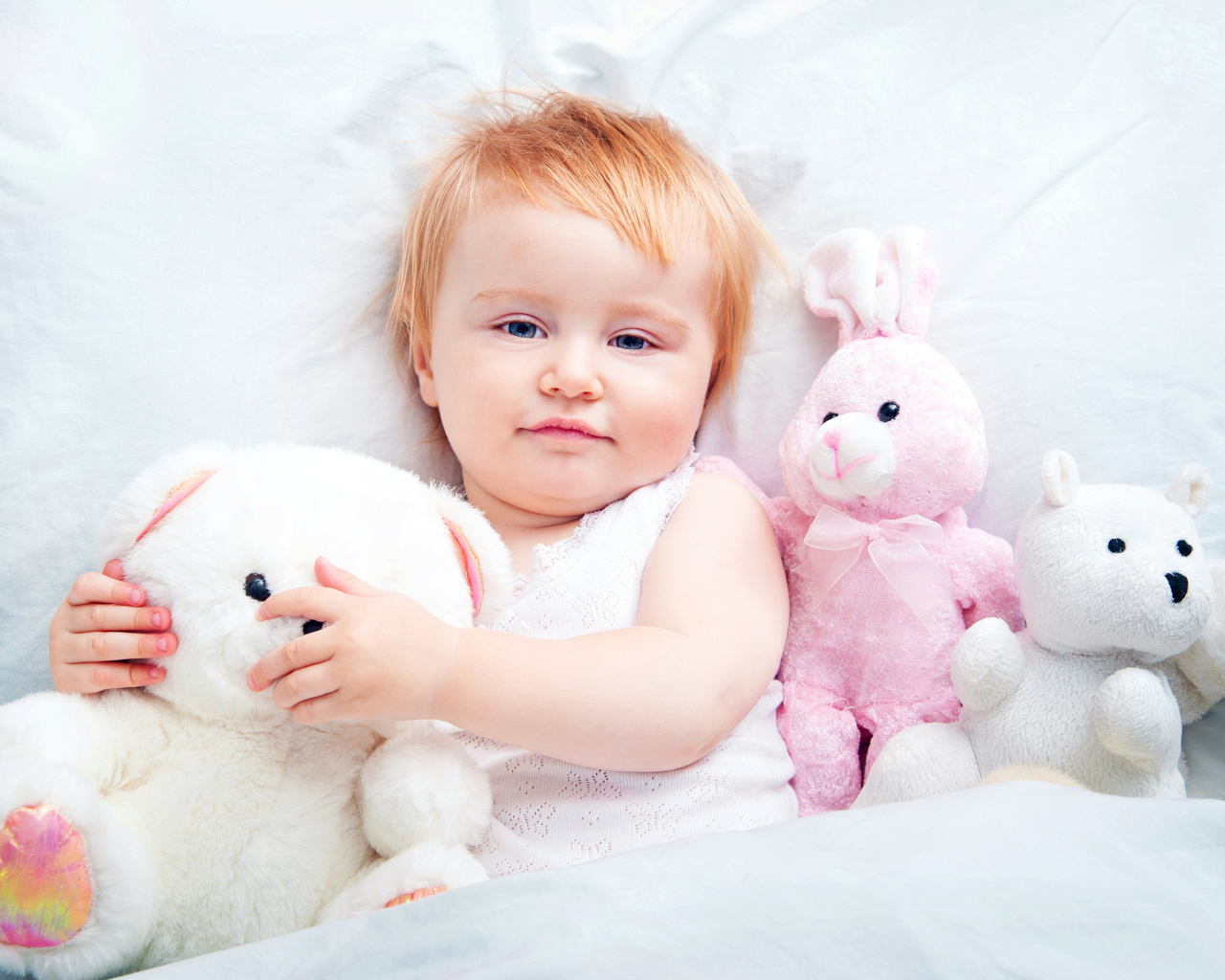 Маленькая девочка лежит в кровати с плюшевыми игрушками