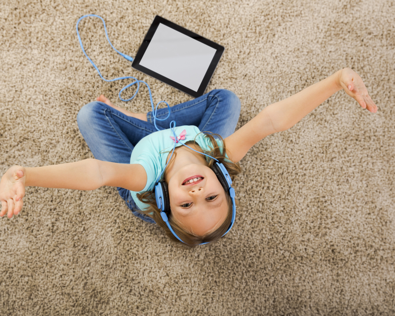 Маленькая девочка слушает музыку в наушниках сидя на ковре