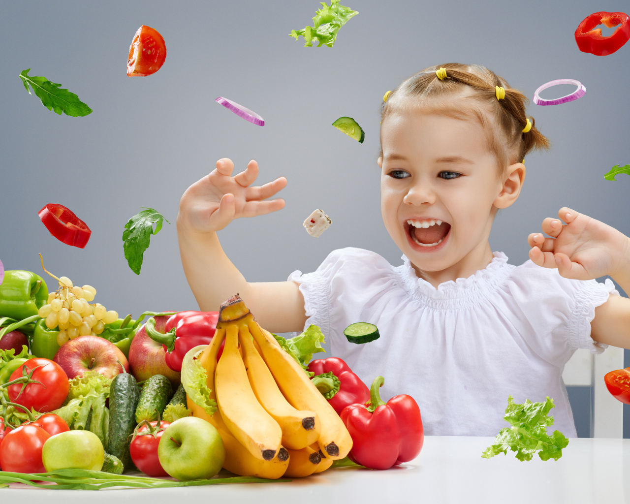 Маленькая девочка играет с овощами и фруктами на кухне
