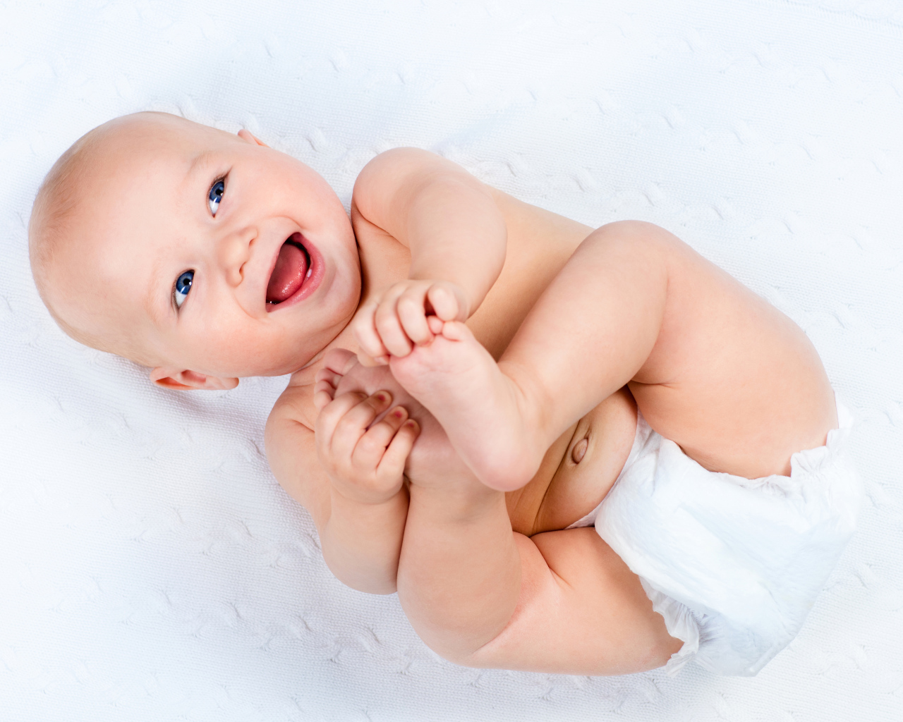 Маленький улыбающийся грудной ребенок держит руками ноги