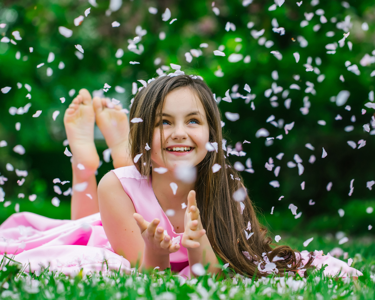 Маленькая улыбающаяся девочка шатенка ловит лепестки