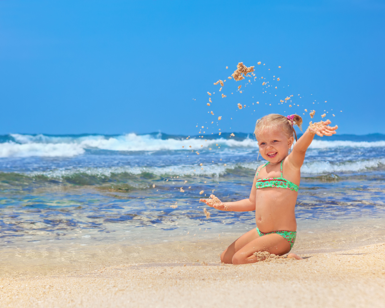 Маленькая улыбающаяся девочка играет на пляже с песком