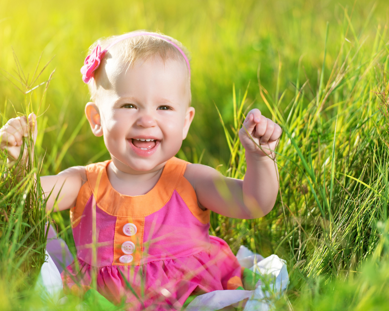 Маленькая улыбающаяся девочка сидит в зеленой траве